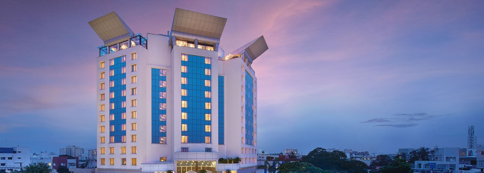 An image of a facade surrounded by trees, with cars parked in the front yard at Accord Hotels and Resorts, one of the top 5-star hotels in Chennai.